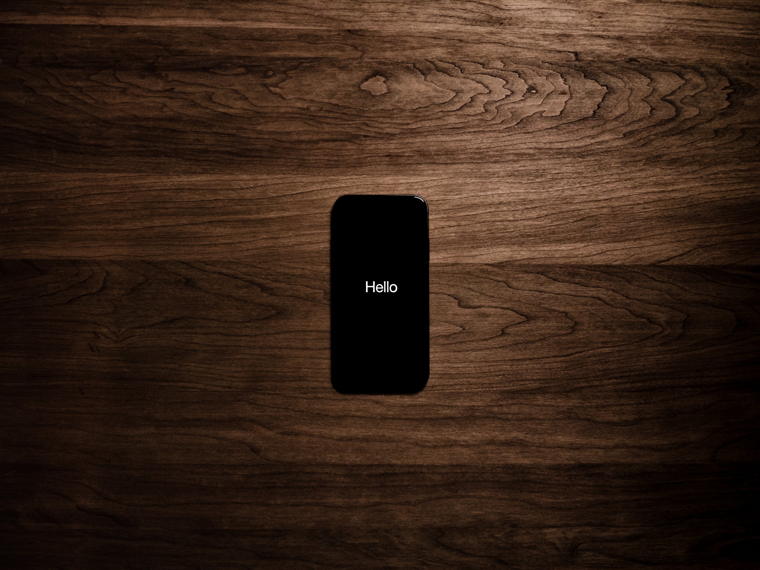 Ein Handy auf dem Hello steht und das auf einem Holztisch liegt.